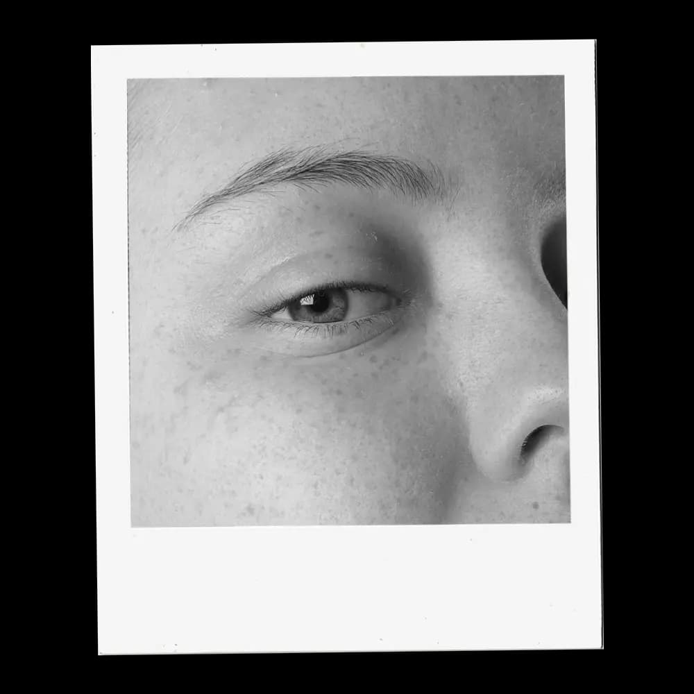 A close-up, black and white photograph captures the intricate details of a human eye. The iris, a mesmerizing mix of light and dark tones, surrounds a dark pupil, reflecting subtle highlights. Delicate eyelashes frame the lower eyelid, while the upper lid is partially visible, casting a soft shadow. Above the eye, a well-defined eyebrow adds structure to the face. The surrounding skin shows fine texture and subtle shading, emphasizing the eye as the focal point.